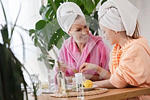 Mother and daughter in bathrobes and towels on head using natural cosmetics and having fun together at home