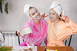 Mother and daughter in bathrobes and towels on head using natural cosmetics and having fun together at home