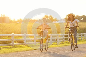 Mother and daughter with bicycling at the garden meadow in sunset near white fence
