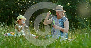 Mother and daughter blow soap bubbles in the park.