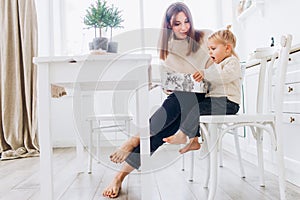 Mother and daughter in a bright kitchen. Homeliness. Joyful baby and his mom.