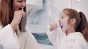 Mother and daughter brush teeth.