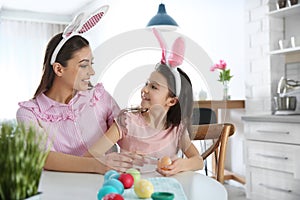 Mother and daughter with bunny ears headbands painting Easter eggs in kitchen