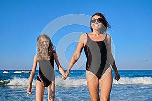 Mother and daughter child walking together on beach holding hands