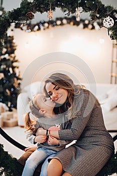 Mother and daughter on Christmas swing. Christmas tree.