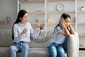 Mother daughter conflict. Young korean mother trying to speak to her upset daugter, sitting on sofa at home