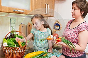 Mother and daughter cooking. Basket of vegetables and fresh fruits in kitchen interior. Parent and child. Healthy food concept