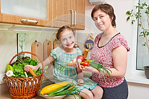 Mother and daughter cooking. Basket of vegetables and fresh fruits in kitchen interior. Parent and child. Healthy food concept