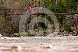 Mother and daughter crossing a suspension bridge across a river.