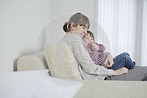 Mother And Daughter Cuddling On Sofa