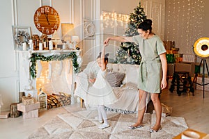 mother and daughter dance at Christmas tree and fireplace with socks for gifts