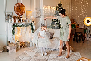 mother and daughter dance at Christmas tree and fireplace with socks for gifts