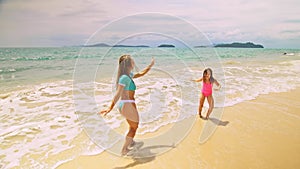 Mother with daughter dancing on shallow water sea. Woman with her girl child enjoying her vacation on tropical island