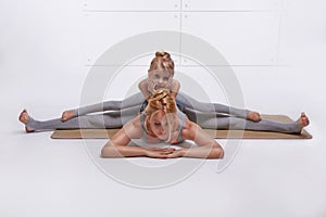 Mother daughter doing yoga exercise, fitness family sports, sports paired woman sitting on the floor stretching his legs apart in