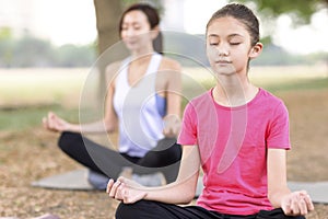 Mother and daughter doing yoga exercises on grass in the park