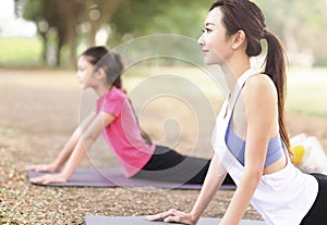 Mother and daughter doing yoga exercises on grass in the park