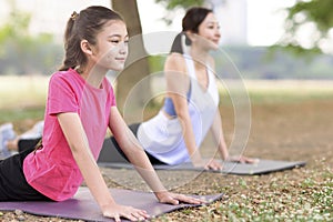 Mother and daughter doing yoga exercises on grass in the park