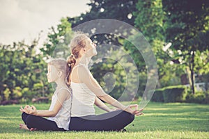 Mother and daughter doing yoga exercises on grass in the park.