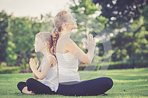 Mother and daughter doing yoga exercises on grass in the park.