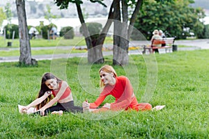 Mother and daughter doing yoga exercises on grass in the park at the day time. People having fun outdoors. Concept of friendly