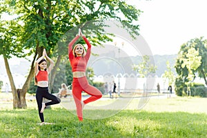 Mother and daughter doing yoga exercises on grass in the park at the day time. People having fun outdoors. Concept of friendly