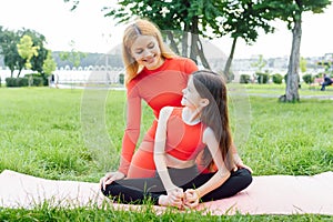 Mother and daughter doing yoga exercises on grass in the park at the day time. People having fun outdoors. Concept of friendly