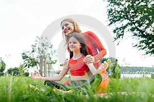 Mother and daughter doing yoga exercises on grass in the park at the day time. People having fun outdoors. Concept of friendly