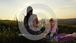 Mother and daughter drawing on a picnic on a hill in the summer at sunset.