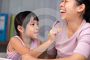 Mother and daughter drawing together with crayons. Adult woman helps girl study or draw together at home in living room. Happy