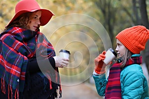 Mother and daughter drink coffee autumn park