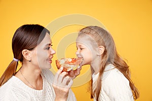 Mother and daughter eating pizza together and having fun iolated over the yellow studio.