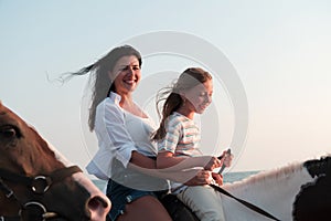 Mother and daughter enjoy riding horses together by the sea. Selective focus