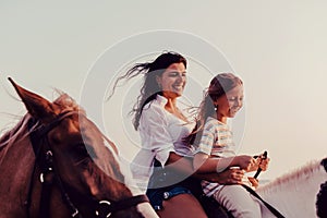 Mother and daughter enjoy riding horses together by the sea. Selective focus