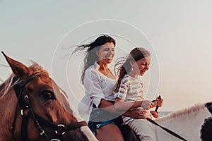 Mother and daughter enjoy riding horses together by the sea. Selective focus