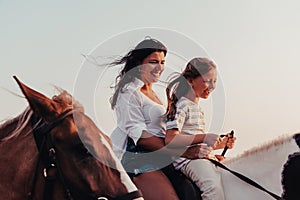 Mother and daughter enjoy riding horses together by the sea. Selective focus