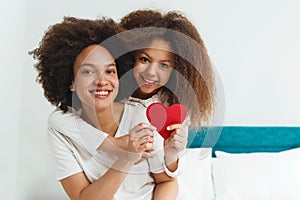 Mother and daughter enjoying on the bed, holding red hearts
