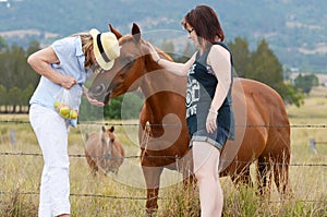 Mother & daughter enjoying day together feeding horses in country