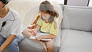 Mother and daughter enjoying family love, sitting together on the living room sofa, working online and drawing in a notebook at