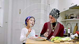 Mother with daughter enjoying salad of fresh vegetables at the dinner table. Mom and daughter eating in the kitchen. Social distan