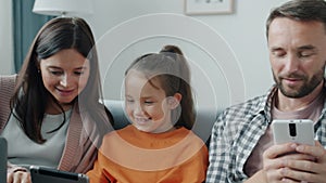 Mother and daughter enjoying tablet laughing while father using smartphone texting at home