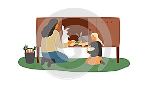 Mother and daughter feeding rabbits in the cell with carrot. Rural farm scene with cute domestic animals and people