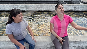 mother and daughter feeding trout in a pond