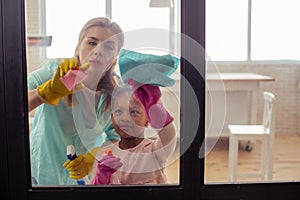 Mother and daughter feeling busy while cleaning the glass door