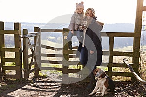 Mother and daughter by a gate in countryside with pet dog