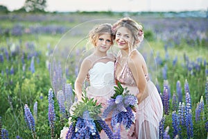 Mother and daughter gathering lupine flowers in beautiful field on sunset. Beautiful girl in violet dress holding a lupine at suns