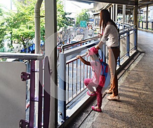 Mother and daughter gaze from an elevated walkway at the street below.