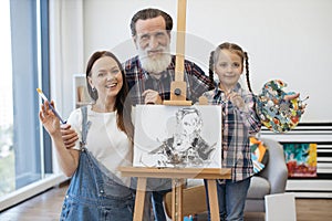 Mother, daughter and granddad posing near easel and smiling