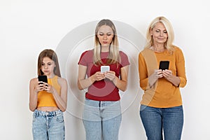 Mother, daughter, grandmother holding phones while posing on white background