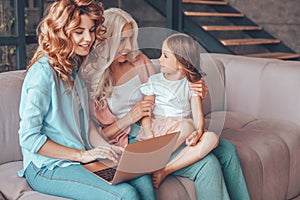 Mother, daughter and grandmother sitting on the couch and using laptop together