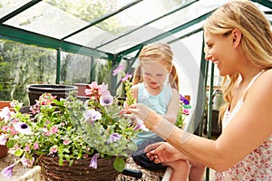 Mother And Daughter Growing Plants In Greenhouse